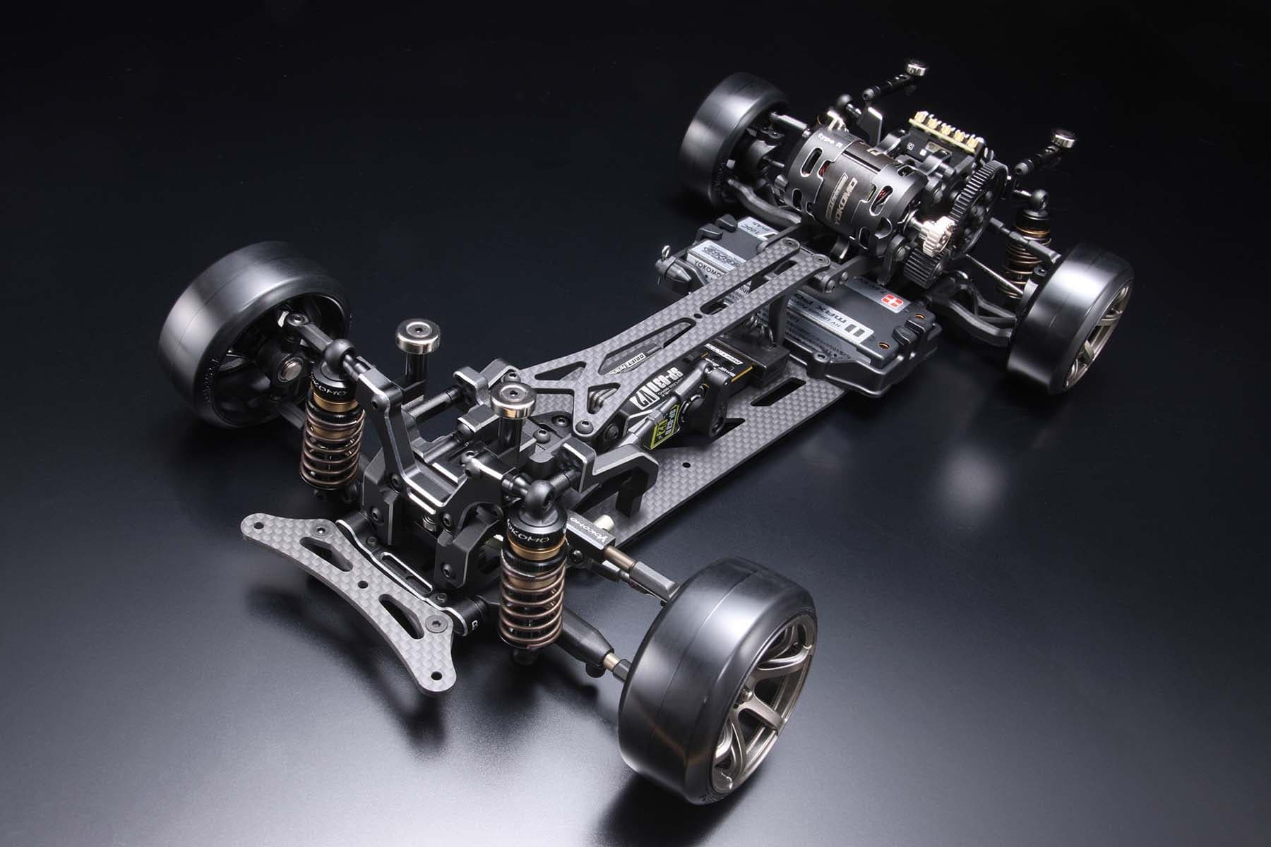 A Yokomo MD3.0 rear-wheel-drive drift chassis without its body, on a black studio floor: graphite decks, gold-bodied shocks, electronics along the middle, and the motor and spur gear mounted high at the rear.